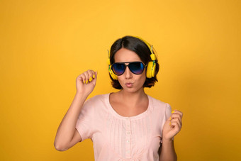 年轻的美丽的夫人桃子t恤听音乐穿耳机太阳镜跳舞孤立的黄色的背景音乐概念技术概念时尚概念