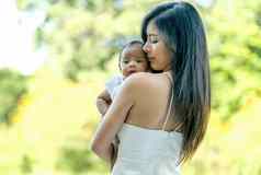 年轻的亚洲美丽的妈妈。携带婴儿婴儿向前绿色花园早....光