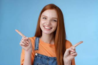 友好的快乐笑漂亮的红色头发的人女孩女学生显示很多机会建议使选择指出横盘整理左<strong>介绍</strong>产品咧着嘴笑很高兴<strong>蓝色</strong>的背景