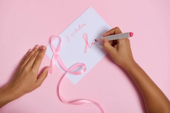 前视图女人的手持有记号笔写10月吸引了纸粉红色的象征乳房<strong>癌症</strong>意识月粉红色的丝带没完没了的结束说谎粉红色的背景