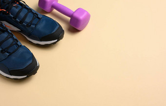 一对蓝色的运动鞋紫色的哑铃米色背景体育复制空间