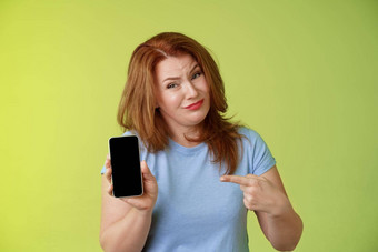 可怕的不高兴失望红色头发的人成熟的女倾斜头畏缩扮鬼脸不情愿的指出智能手机空白显示指数手指显示坏照片分享负的意见