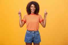 向前乐观雄心勃勃的时尚的皮肤黝黑的女学生条纹很酷的t恤短裤提高手指出向上微笑友好的橙色墙
