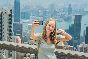在<strong>香港香港维多利亚</strong>峰女人采取自拍坚持图片照片智能手机享受视图<strong>维多利亚</strong>港口查看平台前峰塔散焦背景旅行亚洲概念