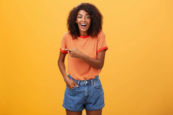女人笑有趣的小狗肖像逗乐娱乐有吸引力的时尚的非裔美国人女休闲牛仔布短裤指出左会说话的太棒了复制空间橙色墙