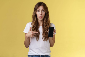 有趣的应用程序检查热情的惊讶有吸引力的女朋友传播流言蜚语朋友的男朋友显示好奇的照片智能手机持有移动电话指出电话屏幕黄色的背景