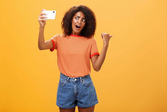 女人记录视频博客指出奇怪的对象肖像有关好奇的时尚的著名的互联网明星持有智能手机会说话的手机相机橙色背景