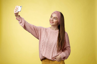 受欢迎的魅力年轻的女互联网生活方式博主采取自拍智能手机扩展手臂采取图片黄色的背景微笑手机屏幕摆姿势厚颜无耻的