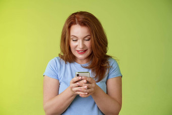 感兴趣兴奋诱人的红色头发的人中年女人购物在线智能手机持有移动电话很高兴娱乐小工具屏幕微笑很高兴玩游戏发现完美的应用程序