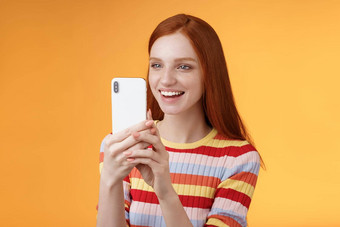 红色头发的人女孩有趣的记录非常滑稽的朋友行动持有智能手机显示逗乐拍摄有趣的<strong>视频</strong>电话站<strong>橙色</strong>背景满意微笑很高兴