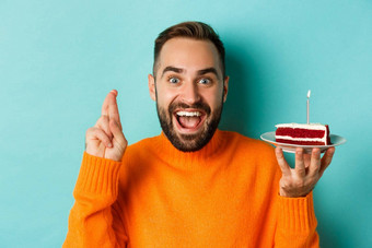 特写镜头快乐成人男人。庆祝生日持有bday蛋糕蜡烛使站绿松石背景