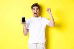 快乐的的家伙显示智能手机屏幕提高手庆祝并互联网成就站黄色的背景