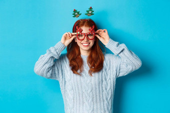 冬天假期圣诞节销售概念美丽的红色头发的人女模型庆祝一年穿有趣的聚会，派对头巾眼镜微笑相机