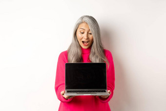 电子商务概念惊讶亚洲祖母灰色头发检查促销在线显示移动PC黑色的屏幕站白色背景