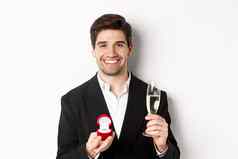 特写镜头英俊的男人。西装使建议给订婚环提高玻璃香槟站白色背景