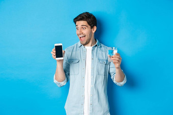 快乐男人。兴奋移动电话屏幕持有玻璃水站蓝色的背景