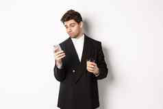 肖像深思熟虑的英俊的商人喝咖啡浏览互联网智能手机屏幕站白色背景
