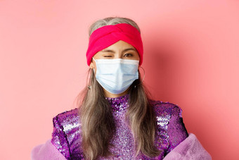 科维德病毒社会距离概念时髦的亚洲高级女人医疗面具闪闪发光的衣服眨眼穿聚会，派对装粉红色的背景
