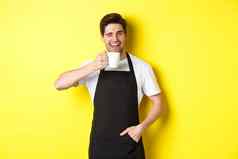 英俊的咖啡师喝杯咖啡眨眼邀请咖啡馆站黄色的背景
