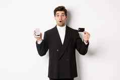 图像英俊的商人黑色的西装惊讶显示信贷卡移动电话屏幕站白色背景