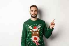 冬天假期圣诞节英俊的有胡子的男人。绿色毛衣指出手指显示促销站白色背景