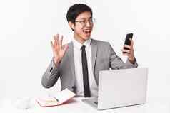 半身照肖像快乐的年轻的亚洲办公室职员坐着表格笔记本移动PC打破说话朋友视频应用穿无线耳机挥舞着屏幕