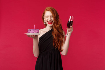 肖像兴奋笑华丽的红色头发的人女人有趣的生日聚会，派对持有玻璃酒生日蛋糕基斯蜡烛使庆祝红色的背景