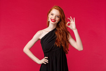 时尚奢侈品美概念肖像满意卖弄风情的漂亮的红色头发的人女人优雅的黑色的衣服显示保证标志很高兴点头微笑快乐红色的背景