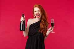 肖像兴奋时髦的无忧无虑的红色头发的人喝醉了女人喝玻璃持有香槟酒瓶大喊大叫有趣的聚会，派对晚上优雅的黑色的衣服红色的背景
