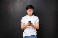 技术小工具人概念惊讶深刻的印象英俊的亚洲的家伙反应令人兴奋的新闻读在线持有移动电话站在智能手机屏幕逗乐