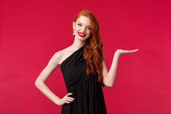 肖像优雅的年轻的红色头发的人女人豪华的黑色的衣服展示持<strong>有产</strong>品手臂红色的背景介绍公司服务微笑相机显示促销