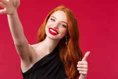特写镜头肖像优雅的令人难以置信的红色头发的人女人红色的口红化妆黑色的衣服显示翘拇指采取自拍推荐太棒了餐厅的地方享受聚会，派对
