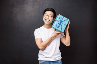 庆祝活动假期生活方式概念兴奋好奇的快乐年轻的亚洲男人。庆祝生日摇晃生日礼物盒子感兴趣什么内部微笑猜测黑色的背景