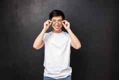 时髦的英俊的年轻的亚洲的家伙挑选规定眼镜眼镜商商店把眼镜自信很高兴相机微笑白色牙齿黑色的背景