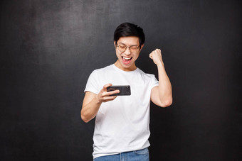 技术小工具人概念快乐快乐的幸运的亚洲的家伙拳头泵庆祝活动持有移动电话微笑并通过了游戏水平黑色的背景