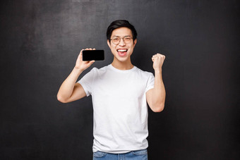 肖像幸运的兴奋亚洲的家伙赢得钱体育运动打赌拳头泵庆祝显示分数移动游戏显示持有智能手机并黑色的背景