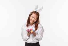 复活节假期庆祝活动概念肖像可爱的愚蠢的年轻的害羞的亚洲女孩兔子耳朵持有画鸡蛋微笑脸红适度的站白色背景