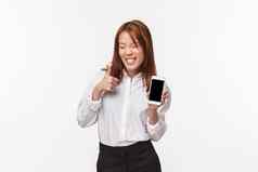 肖像无忧无虑的快乐的满意微笑亚洲女人衬衫裙子显示移动电话显示愚蠢的喜气洋洋的露齿而笑使翘拇指批准白色背景