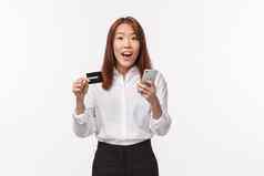 肖像兴奋可爱的亚洲女衬衫裙子持有移动电话信贷卡使互联网订单购物在线银行存款注册账户商店白色背景