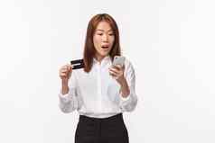 肖像兴奋可爱的亚洲女购物狂订单在线持有移动电话信贷卡智能手机显示插入银行信息站白色背景