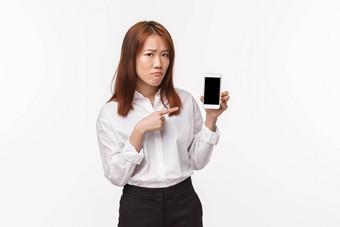 肖像伤心悲观的亚洲女人感觉不安心烦意乱持有移动电话显示指出手指智能手机使不开心陷入困境的表达式白色背景