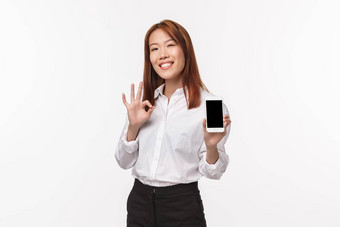 好满意好看的亚洲女人显示移动电话显示使手势率优秀的应用程序感觉骄傲采取很酷的图片站白色背景