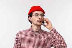 特写镜头肖像年轻的高加索人男人。眼镜红色的无檐小便帽谈话调用朋友搜索人人群持有智能手机耳朵白色背景