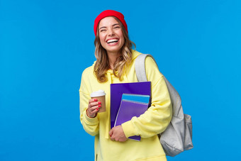 快乐的快乐女学生有趣的享受大学生活方式携带背包笔记本电脑喝外卖咖啡会说话的同学们站蓝色的背景快乐的