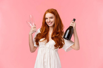 时髦的好看的红色头发的人女人庆祝女<strong>朋友</strong>有趣的持有瓶香槟眼镜<strong>邀请</strong>喝微笑厚颜无耻的快乐站粉红色的背景