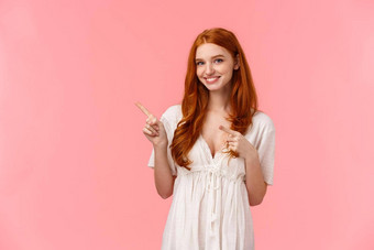 半身照肖像可爱的欧洲红色头发的人女白色时尚衣服指出手指上左角落里邀请退房促销活动给建议粉红色的背景