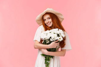 可爱的诱人的浪漫的可爱的愚蠢的红色头发的人女孩太阳稻草他拥抱美丽的白色花收到礼物花束微笑相机厚颜无耻的站卖弄风情的粉红色的背景
