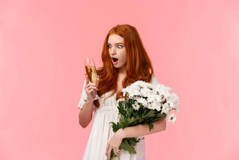 女孩深刻的印象惊讶好香槟口味迷人的红色头发的人女庆祝浪漫的日期holdig白色花束花玻璃喝粉红色的背景