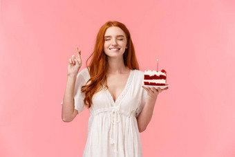 庆祝活动幸福概念有吸引力的梦幻红色头发的人女孩可爱的白色衣服持有生日蛋糕交叉手指好运气咬唇诱人的关闭眼睛使打击蜡烛