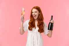 兴奋无忧无虑的喝醉了红色头发的人高加索人女朋友有趣的野生免费的太棒了聚会，派对提高玻璃瓶香槟微笑时髦的站粉红色的背景